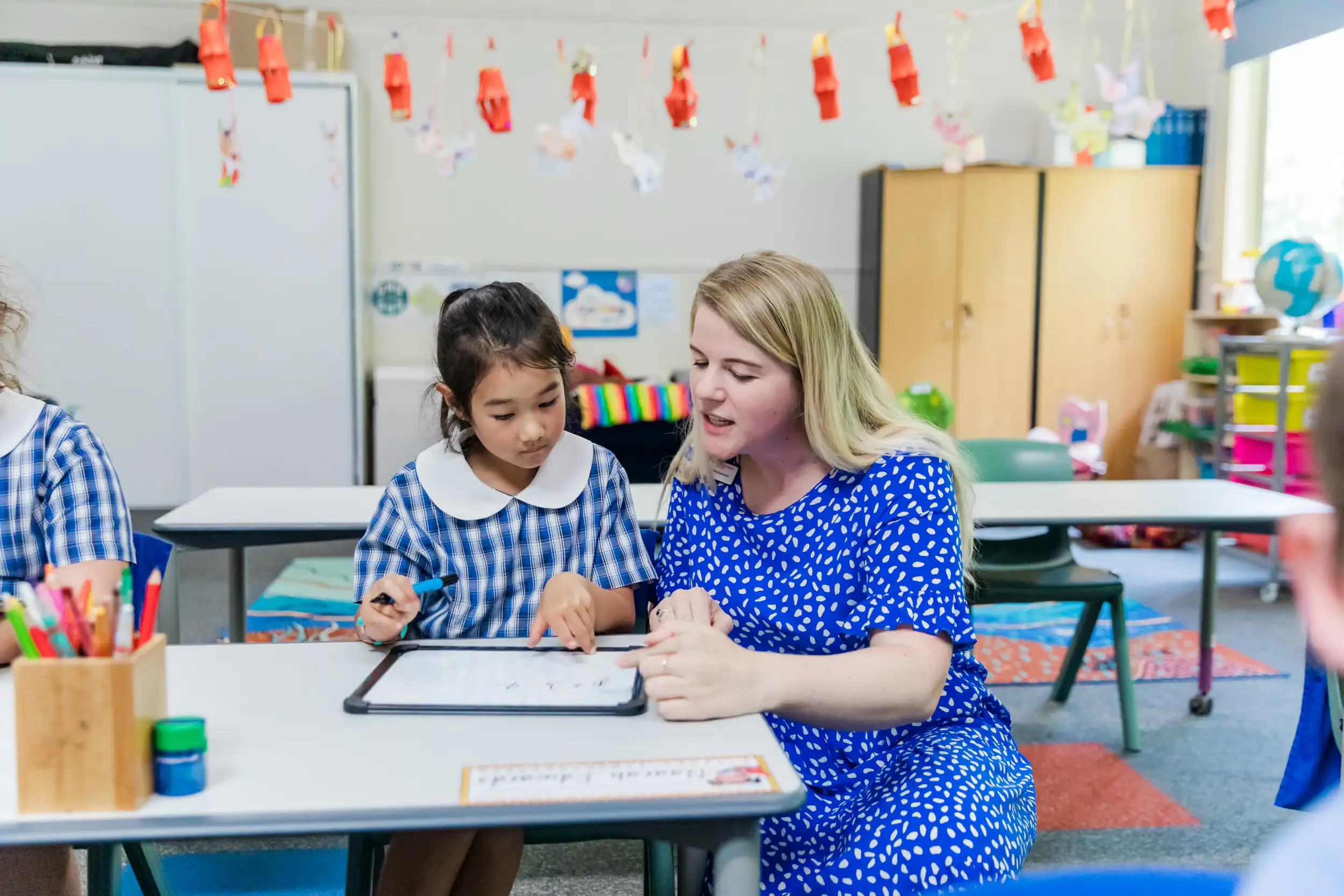 A teacher helping a primary school student use a tablet