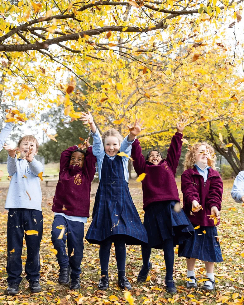 Primary school students throwing autumn leaves outdoors