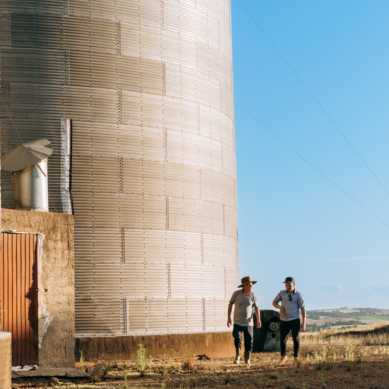 Two people walking beside a grain silo on a farm