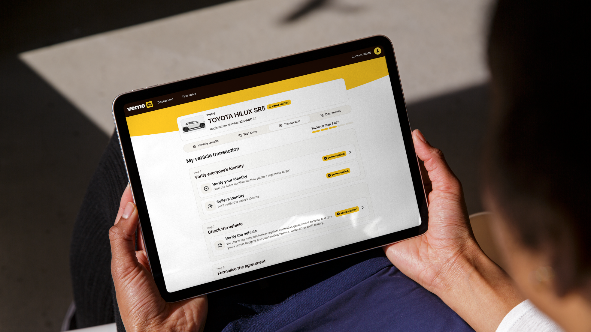 Person holding a tablet showing a VEME vehicle transaction for a Toyota Hilux SR5