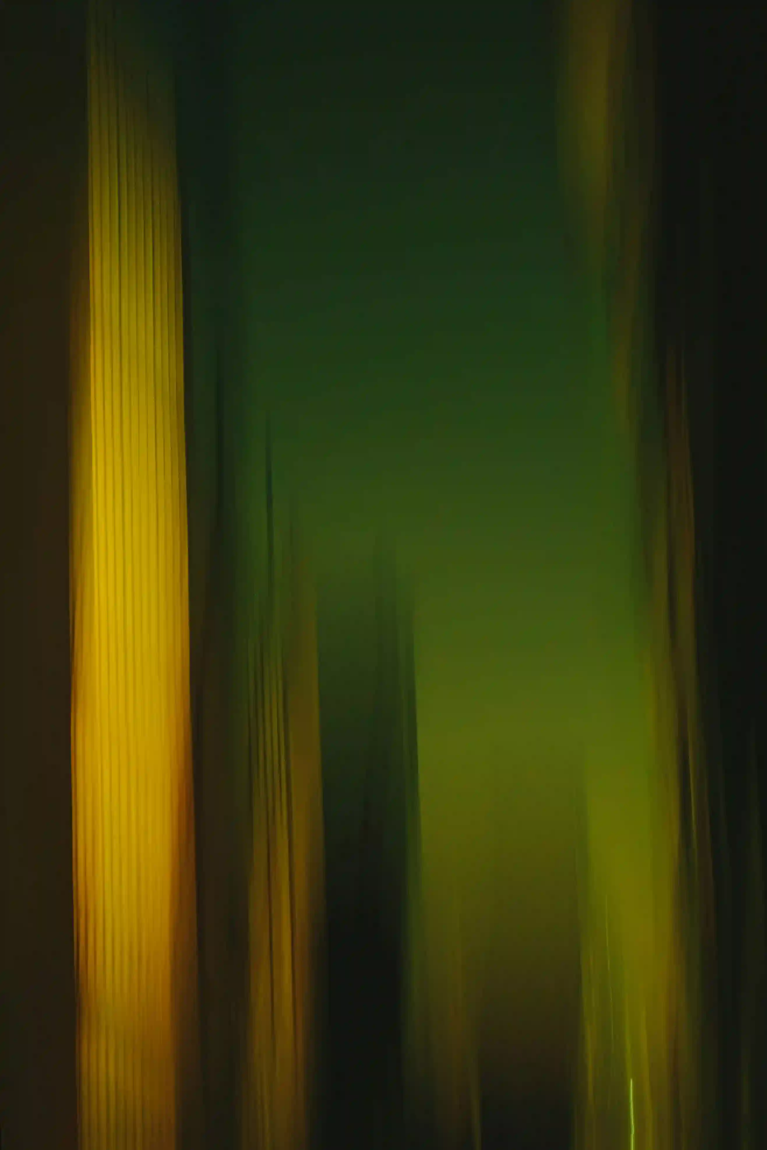 Blurred vertical shapes in green and yellow hues resembling abstract cityscape or light streaks.