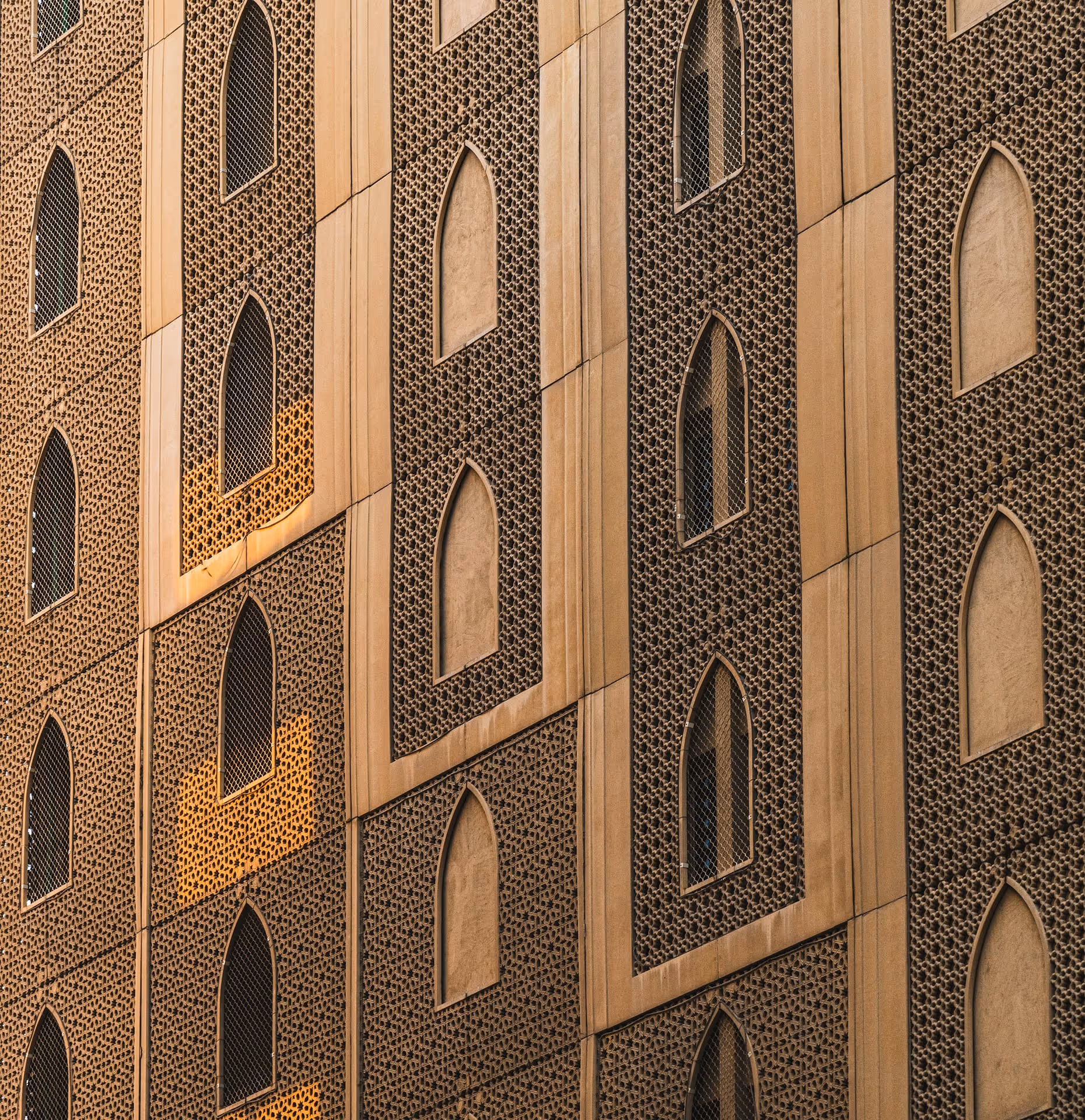 Close-up of a building facade featuring repeating arched windows with lattice patterns and intricate geometric perforations.