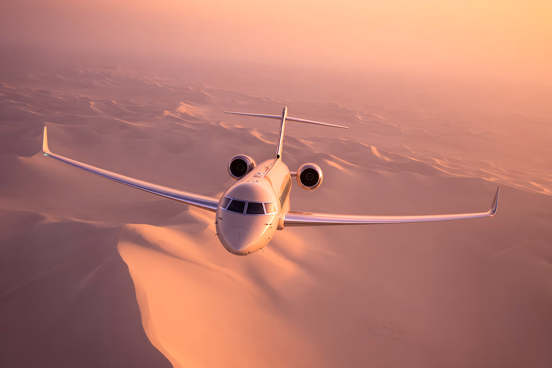 Private jet flying over desert dunes at sunset under soft orange light.