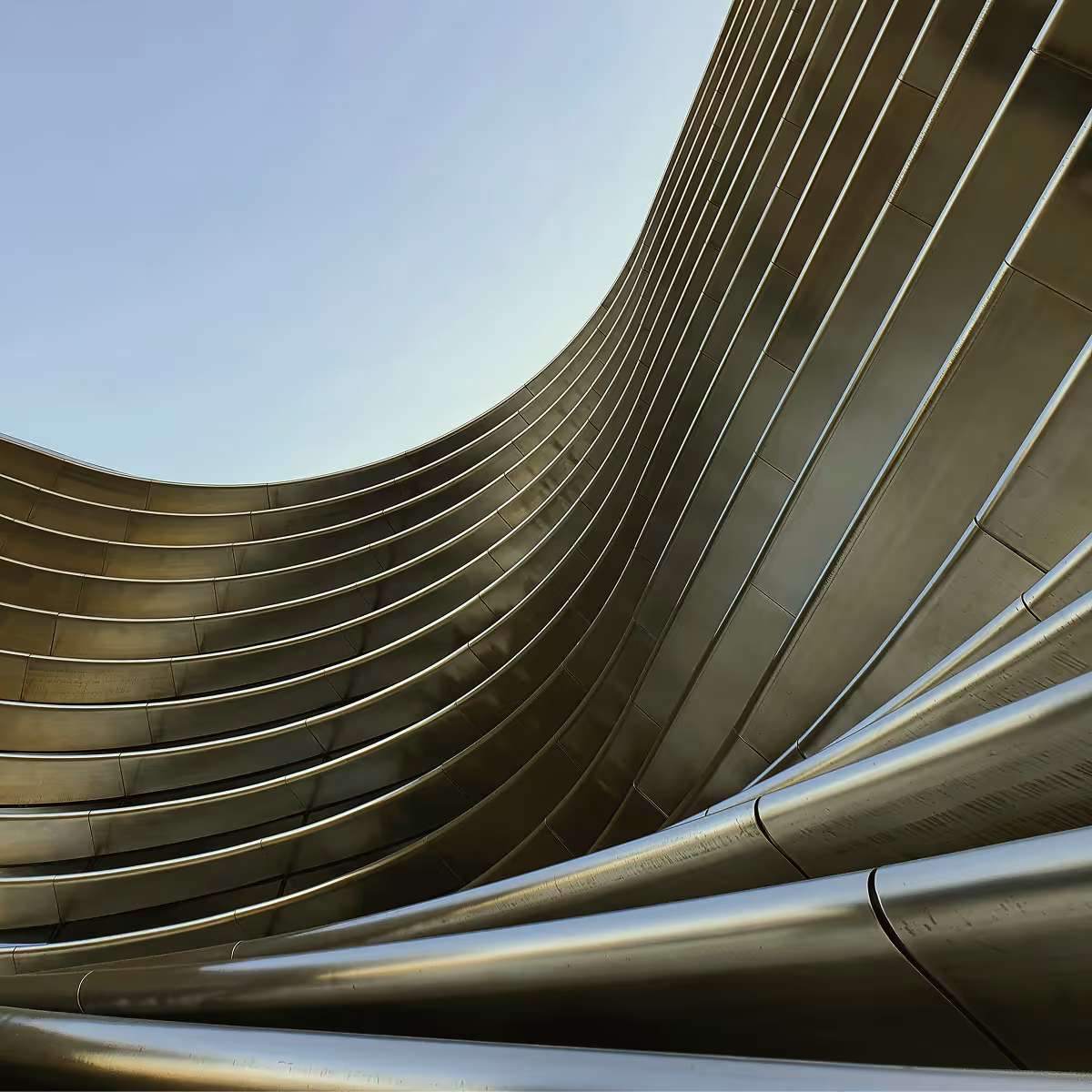 Upward view of a modern building with curved, metallic architectural lines against a clear sky.