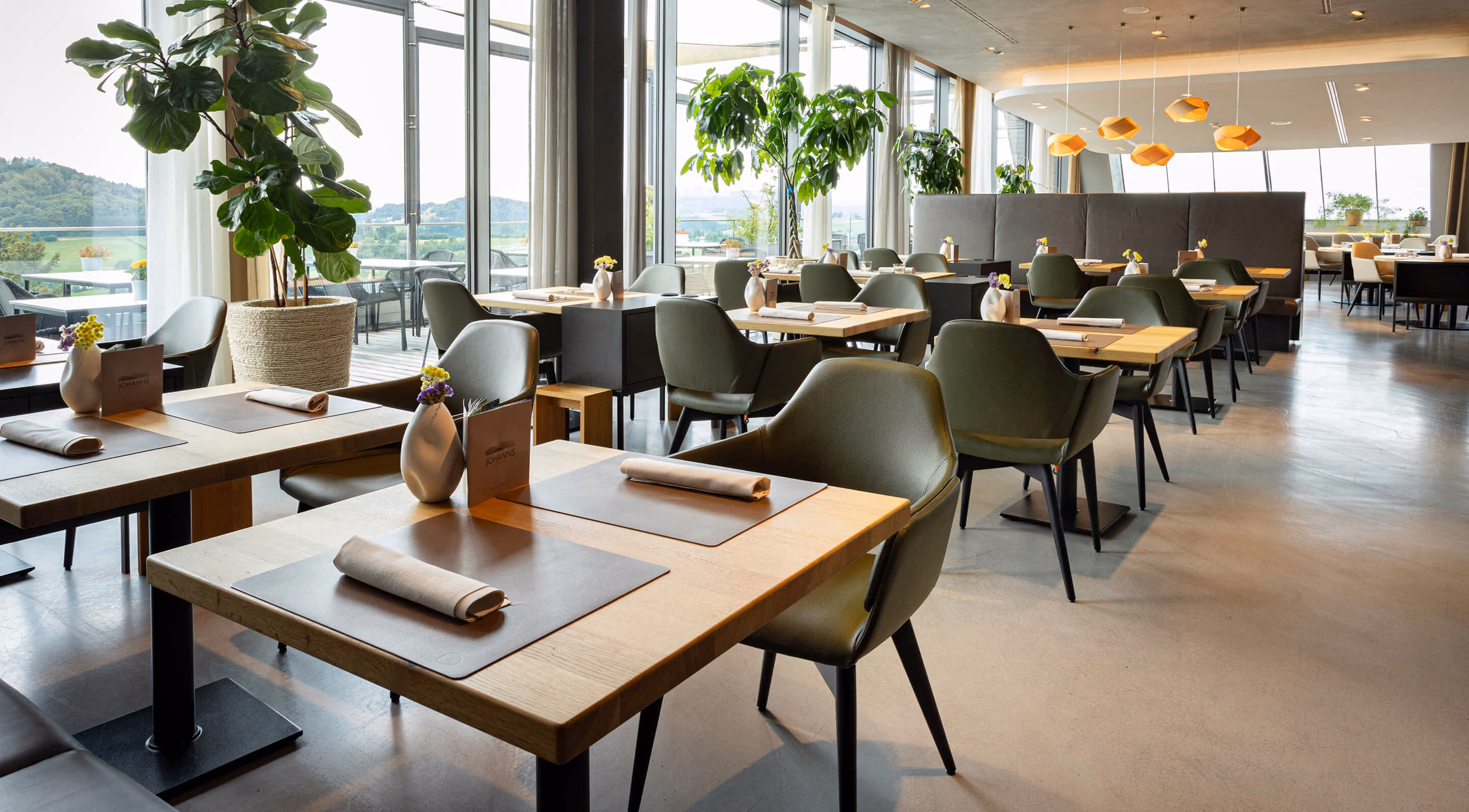 Gastraum des Restaurants JOHANNS mit gedeckten Tischen und Blick ins Grüne