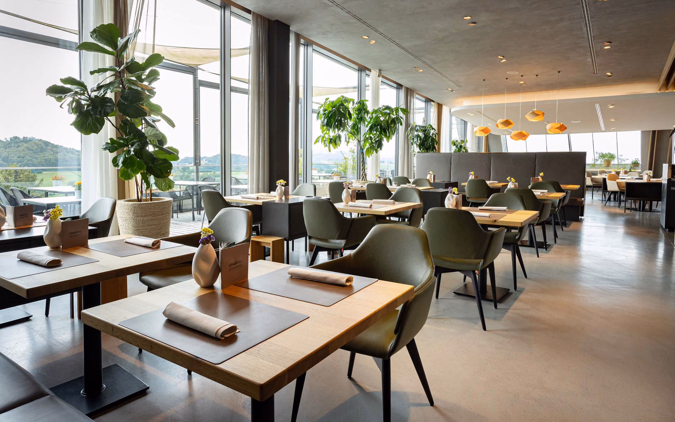 Gastraum des Restaurants JOHANNS mit Pflanzen, gedeckten Tischen und Fensterfront
