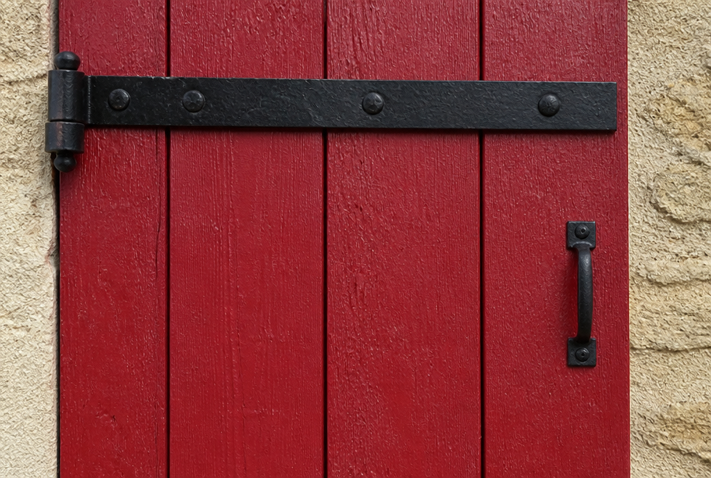 Detail des pentures noires et des lames verticales du volet bois rouge