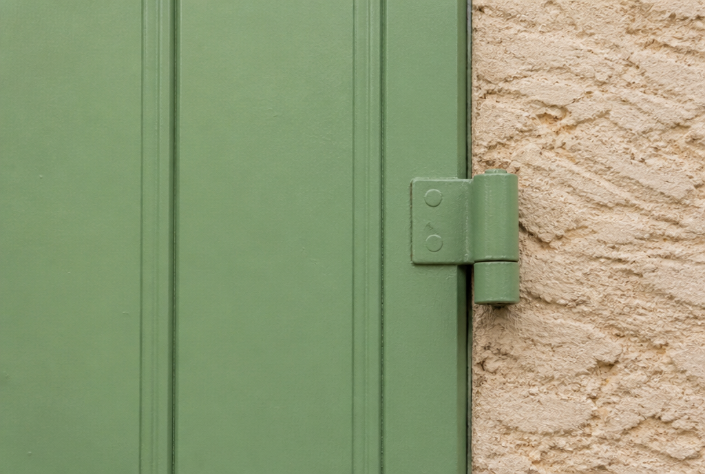 Detail d'un volet aluminium vert, joints verticaux et gond sur le crepi creme texture