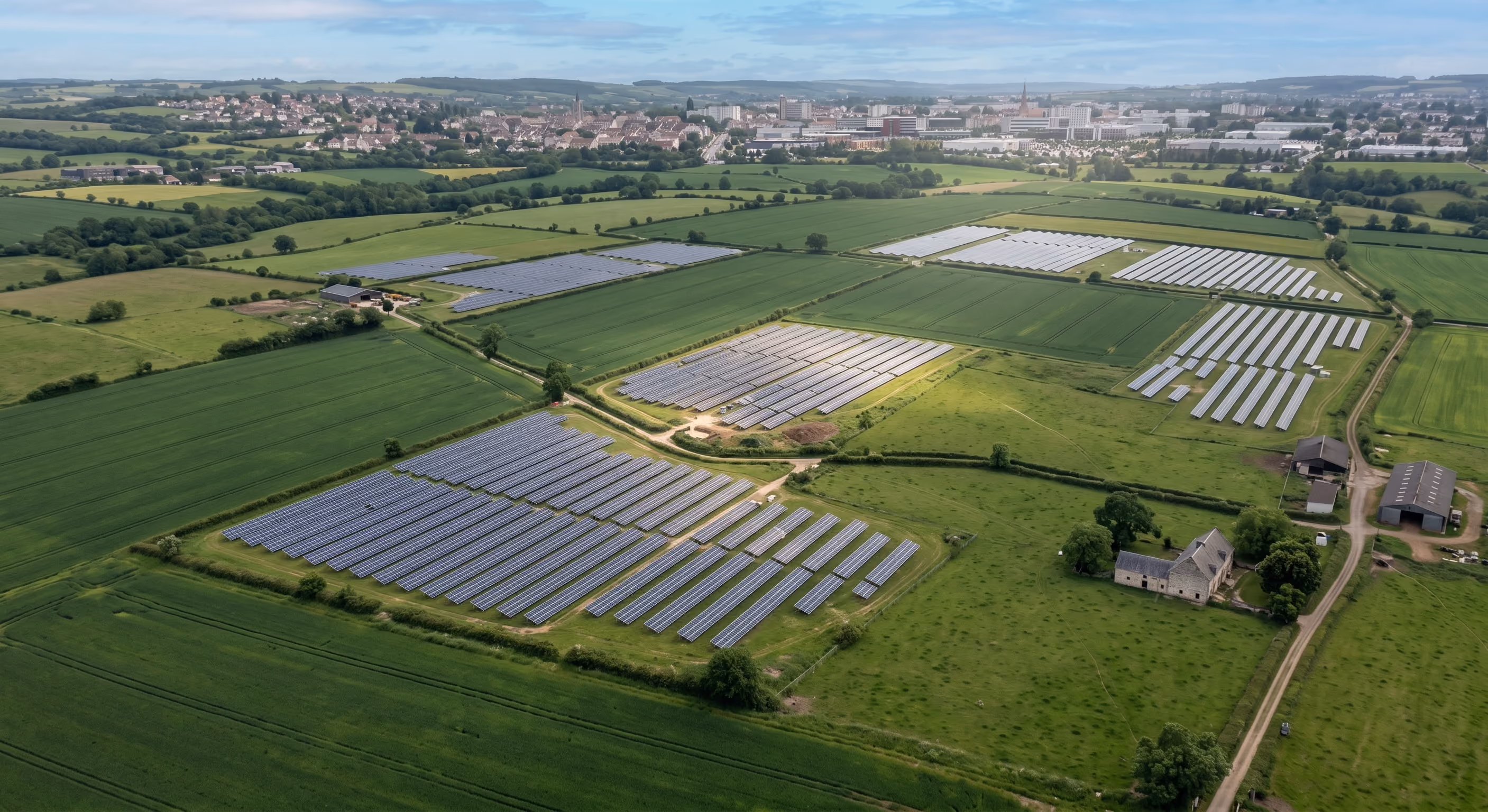 Vue aérienne d'une centrale solaire au sol installée dans un champ, avec des rangées de panneaux au milieu de terres agricoles