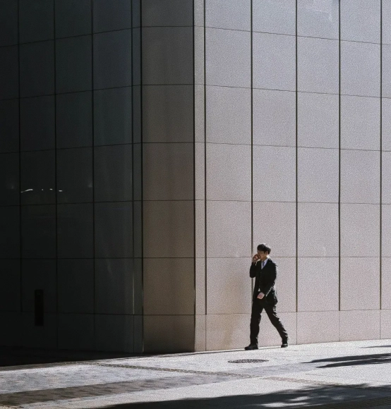 Homme en costume au téléphone longeant la façade d'un immeuble de bureaux