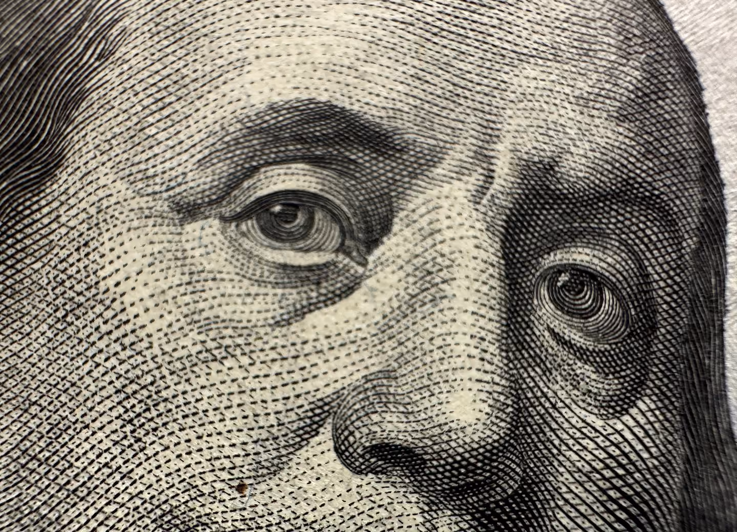 Close-up of Benjamin Franklin’s eyes and nose from a US hundred-dollar bill showing detailed engraving.