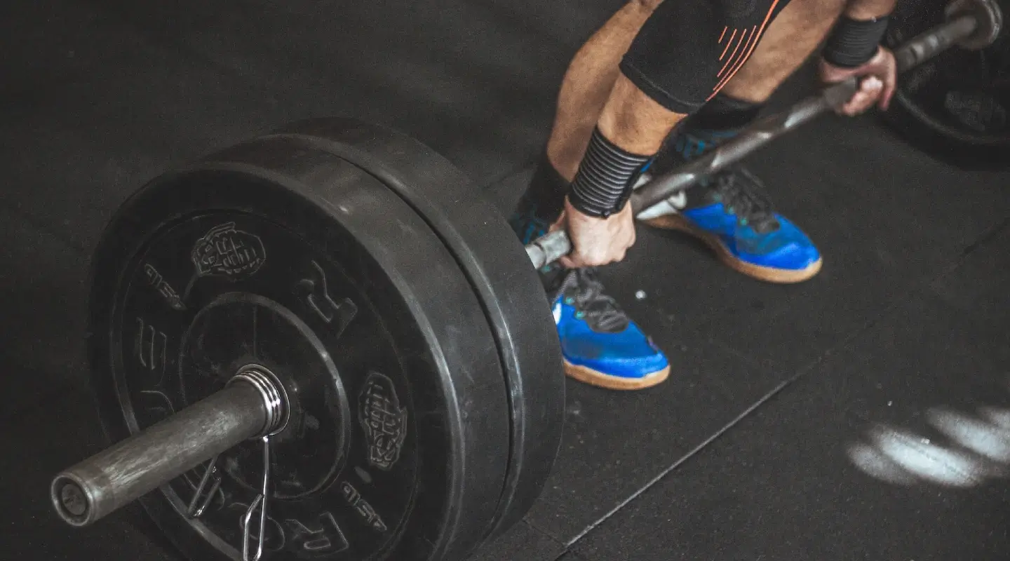 Athlete performing a heavy barbell deadlift with bumper plates during a strength training session at House of Strength in San Diego, CA.