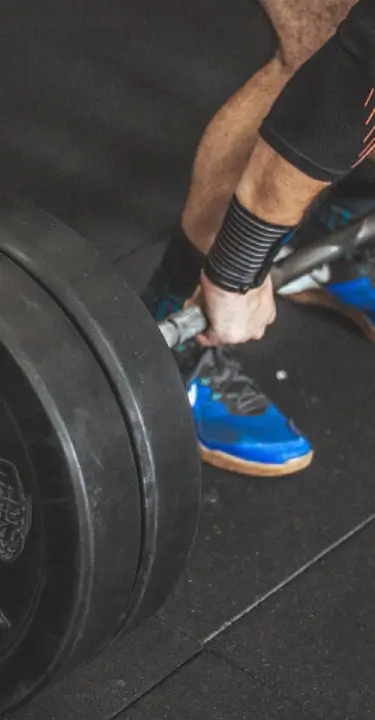 Athlete performing a heavy barbell deadlift with bumper plates during a strength training session at House of Strength in San Diego, CA.