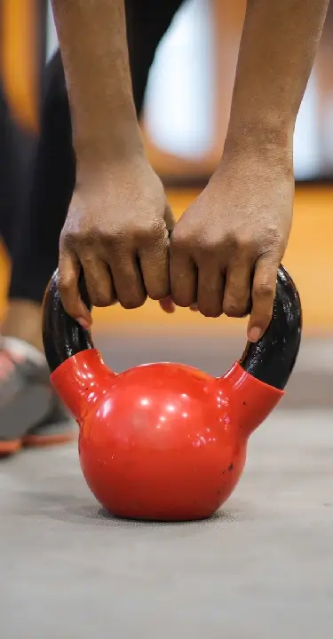 Close-up of an athlete gripping a red kettlebell during a strength training workout at House of Strength in San Diego, CA.