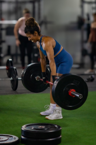 Focused on a determined lifter wearing athletic wear, showing intense effort while performing a heavy deadlift on a green turf floor.