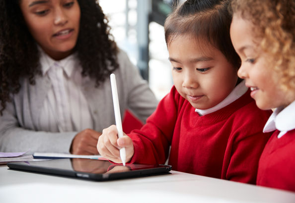 Photo of two young pupils working on a tablet, with an adult supervising