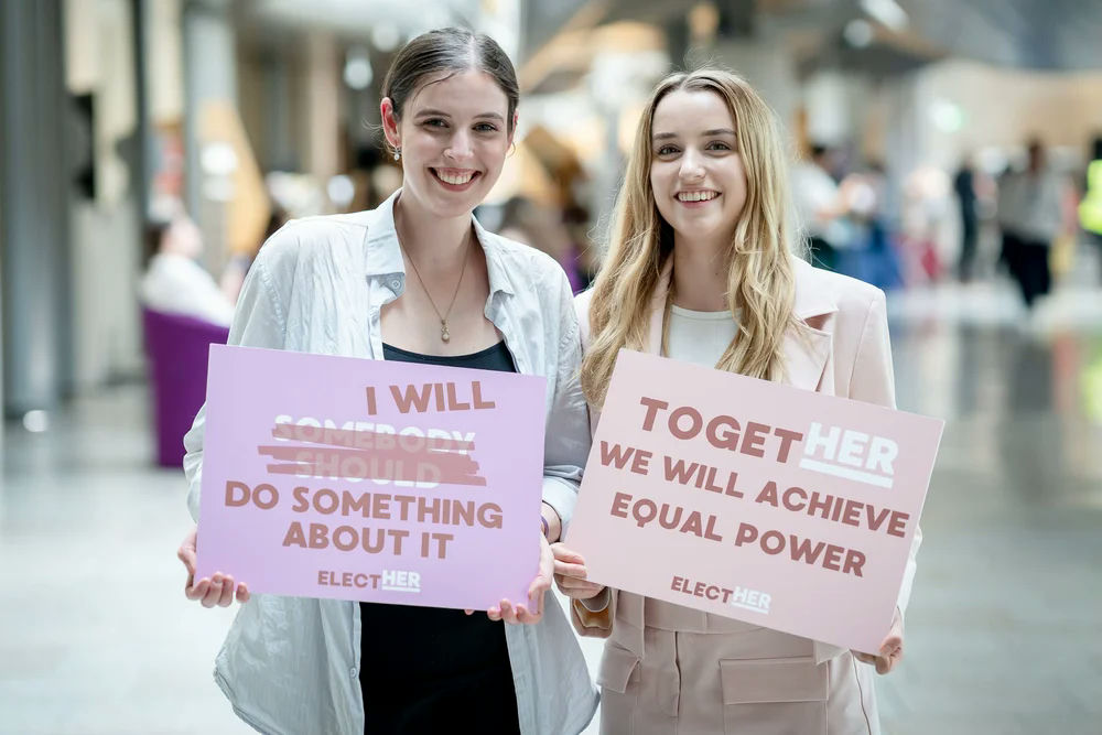 Photo of two women smiling and holding motivational placards
