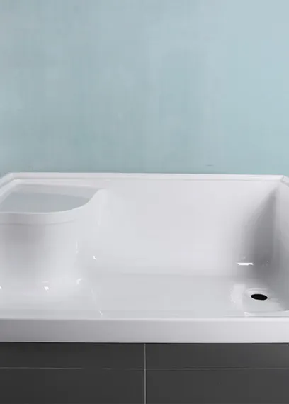 White acrylic bathtub with a built-in seat against a light blue wall.