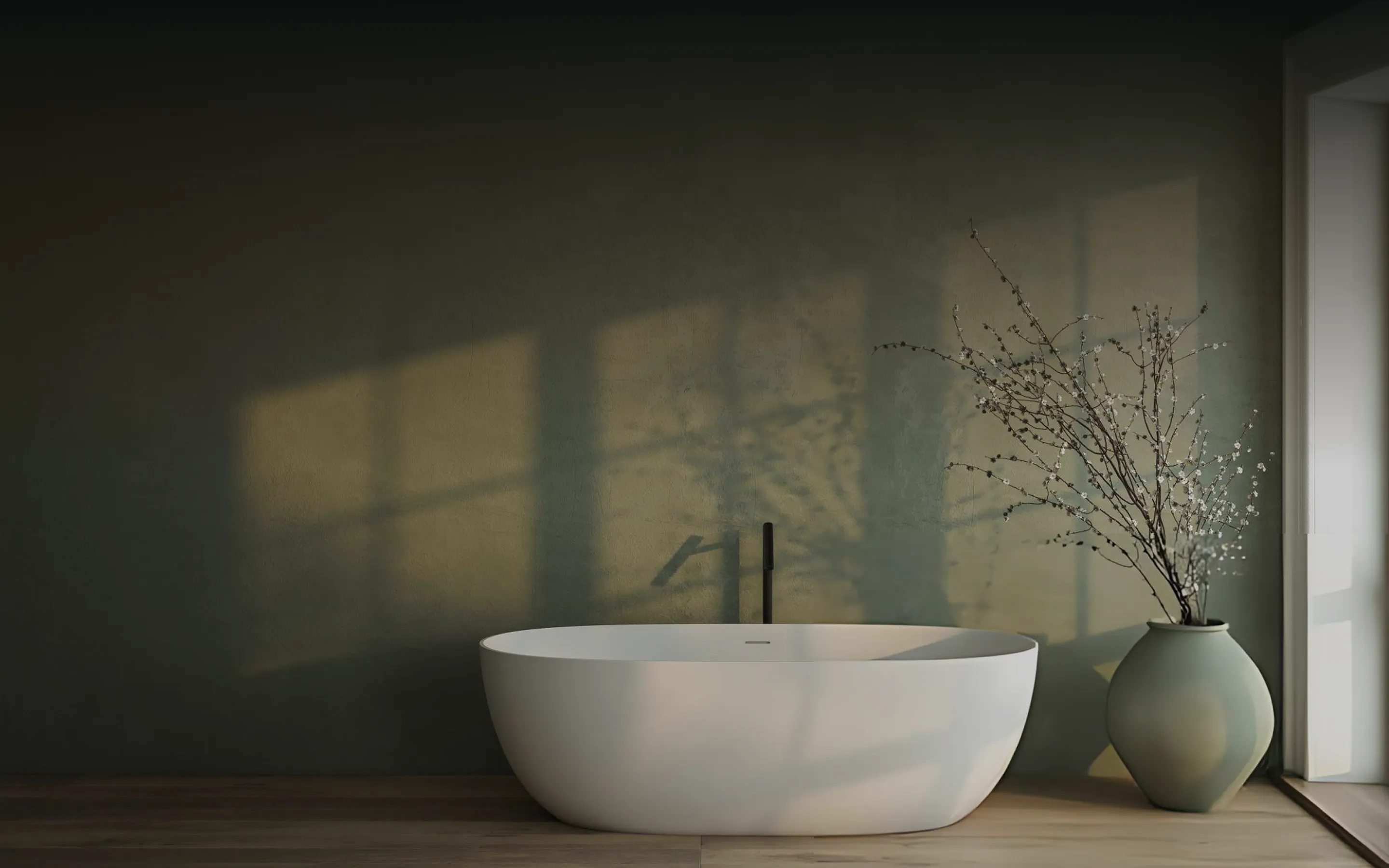 Modern white freestanding bathtub beside a vase with branches near a window with sunlight shadows.