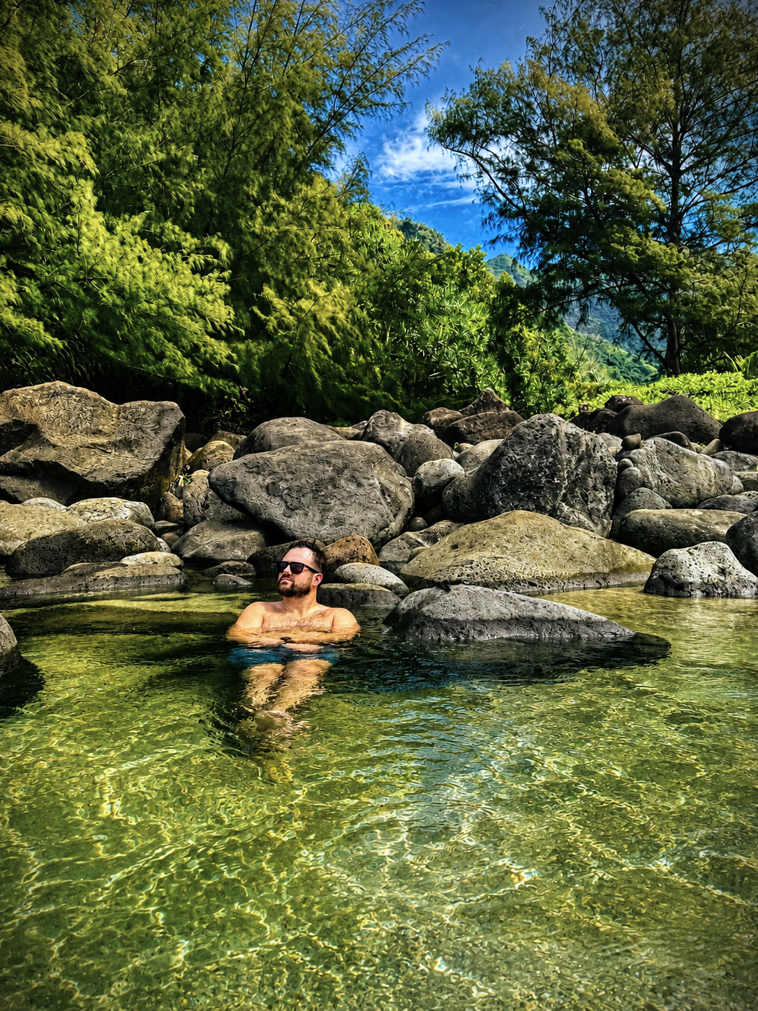Man relaxing in a natural river swimming hole surrounded by boulders in a Kauai jungle.