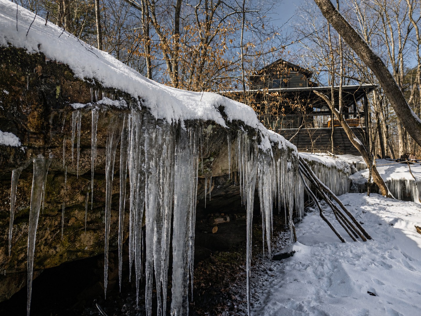 Icicles hanging from a snow-covered rock bluff with the Sleepy Hollow cabin visible in the background.