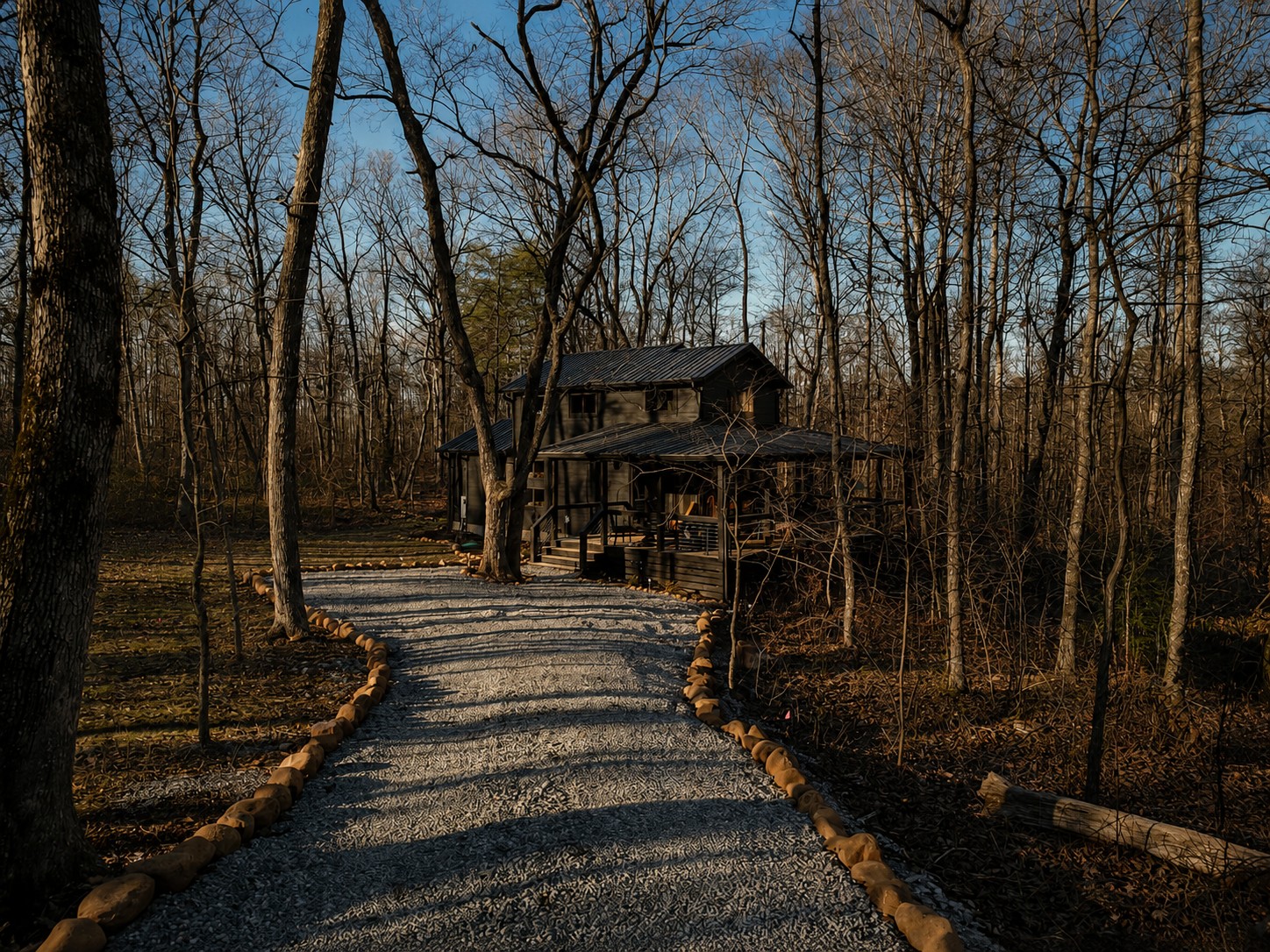 Stone-lined gravel driveway leading through the woods to the Sleepy Hollow cabin at golden hour.