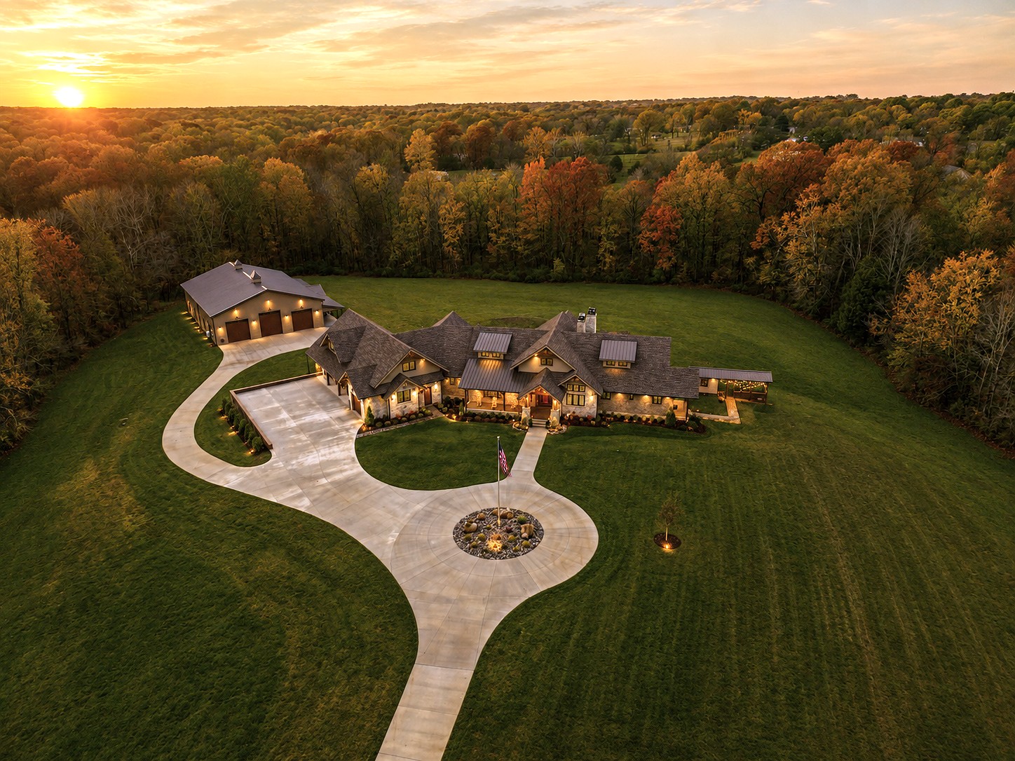 Aerial view of a Hannah Custom Homes estate surrounded by fall foliage, circular driveway lit at sunset.