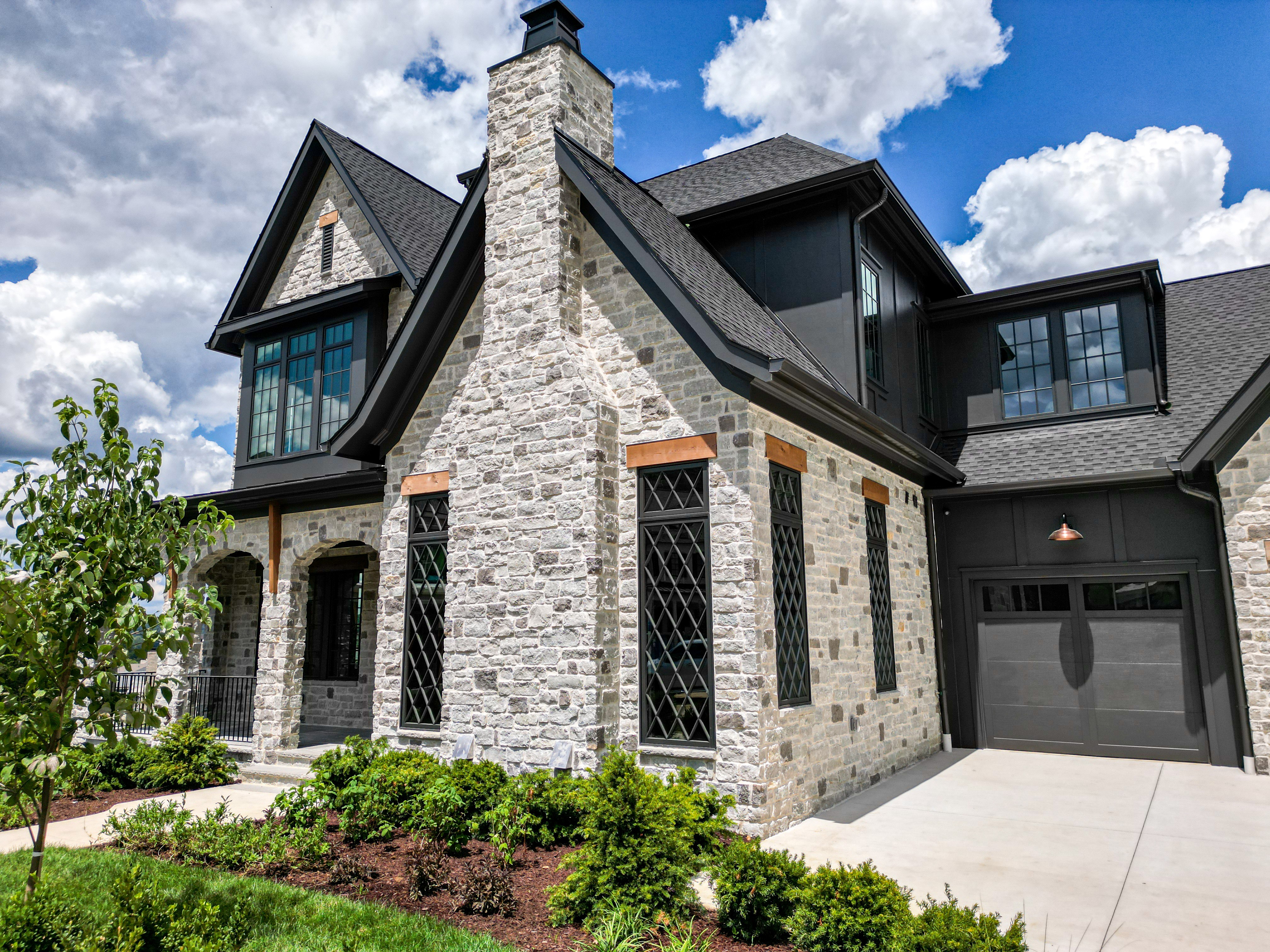 Close-up of a stone-facade home built by Zurich Homes, with a steep gabled roof and dark garage door.