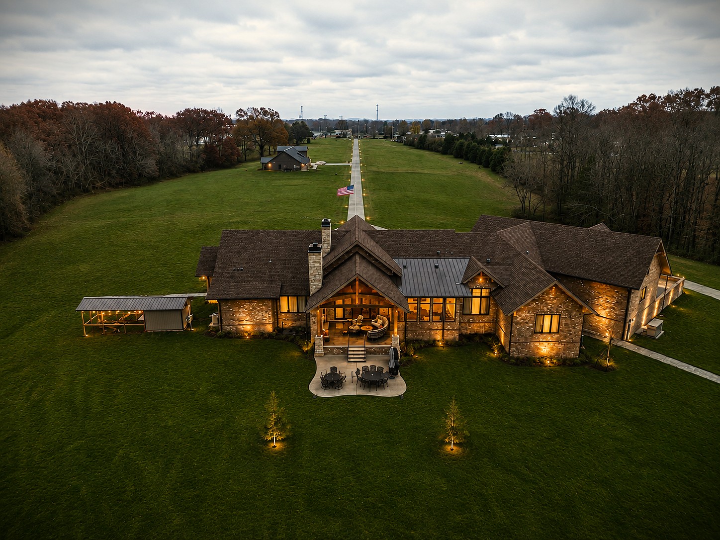 Aerial view of a Hannah Custom Homes estate lit up at dusk with a long tree-lined driveway.