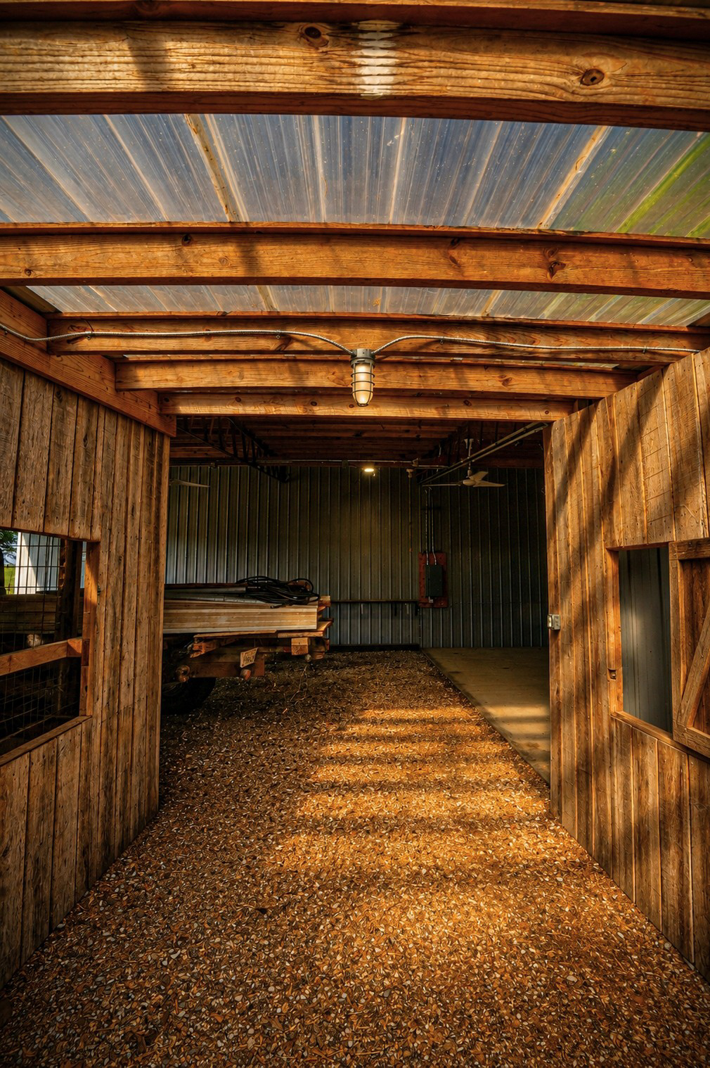 View down the barn's center aisle toward the workshop bay and the lumber-loaded flatbed truck.