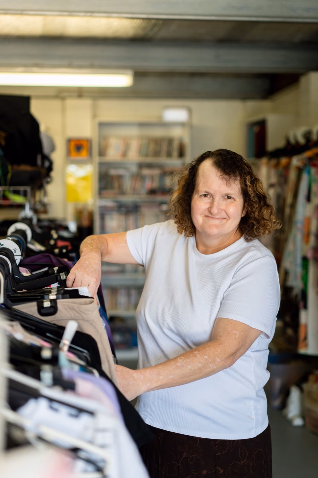 A woman smiling while sorting clothing at a community op shop