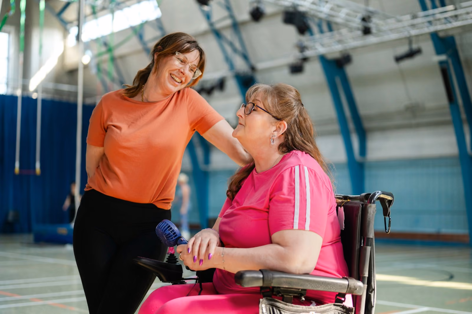A support worker and participant laughing together at a sports centre