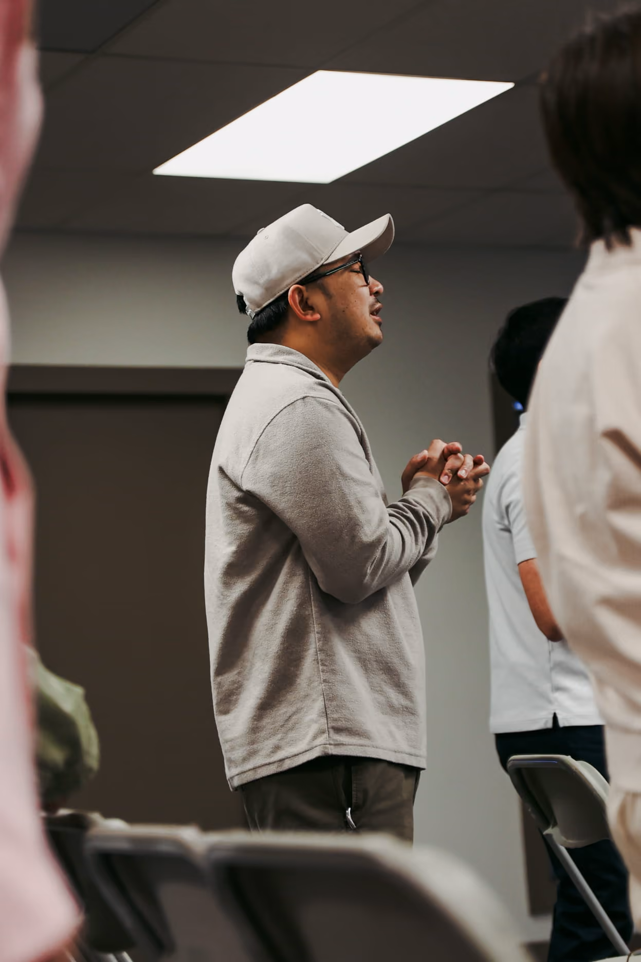 An image of a man wearing a baseball cap praying while standing up and hands together.
