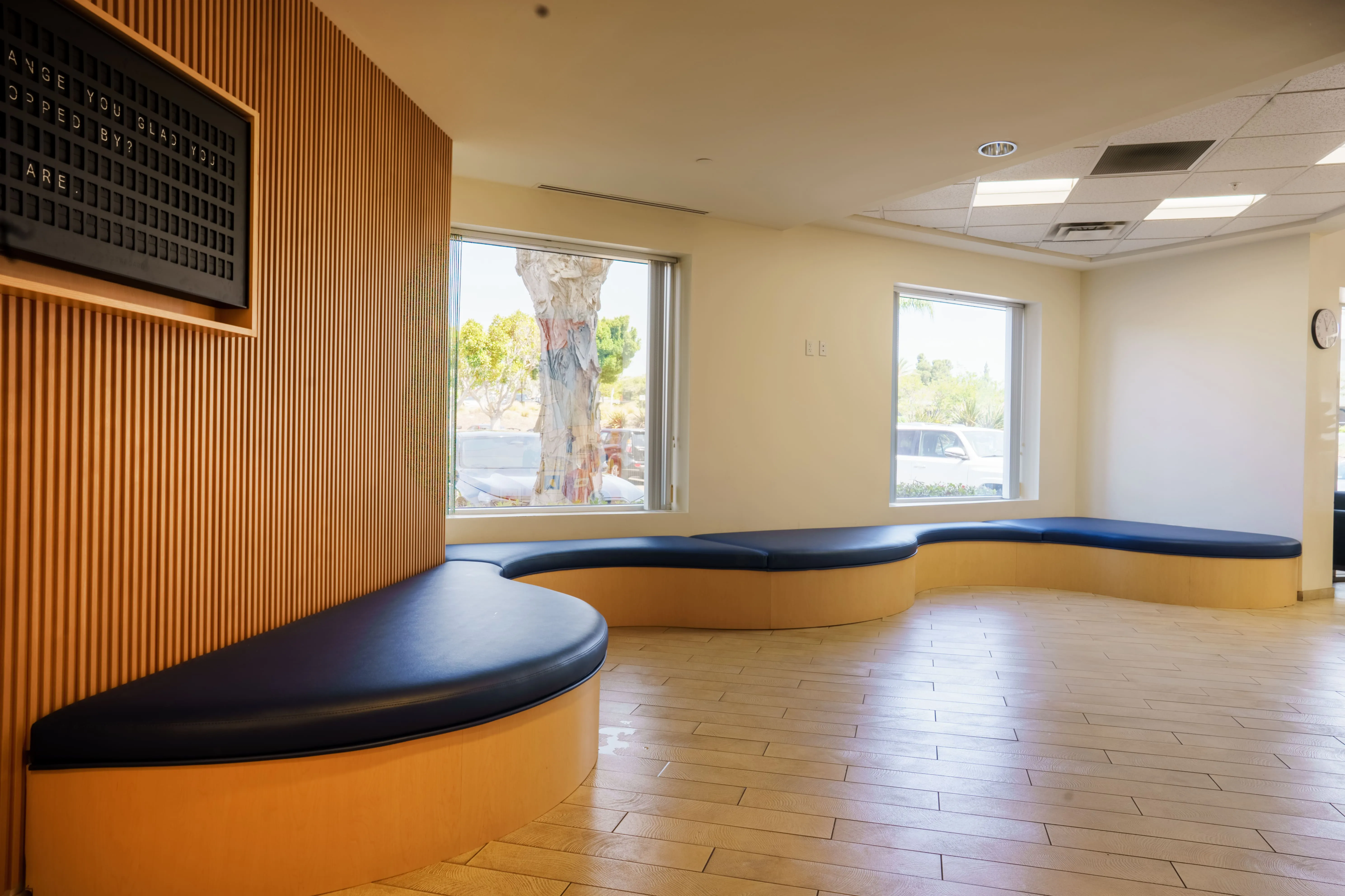 Curved wood-and-navy bench seating along a wood-slat wall in Feeding San Diego's lobby, with a digital message board and a window overlooking the parking lot