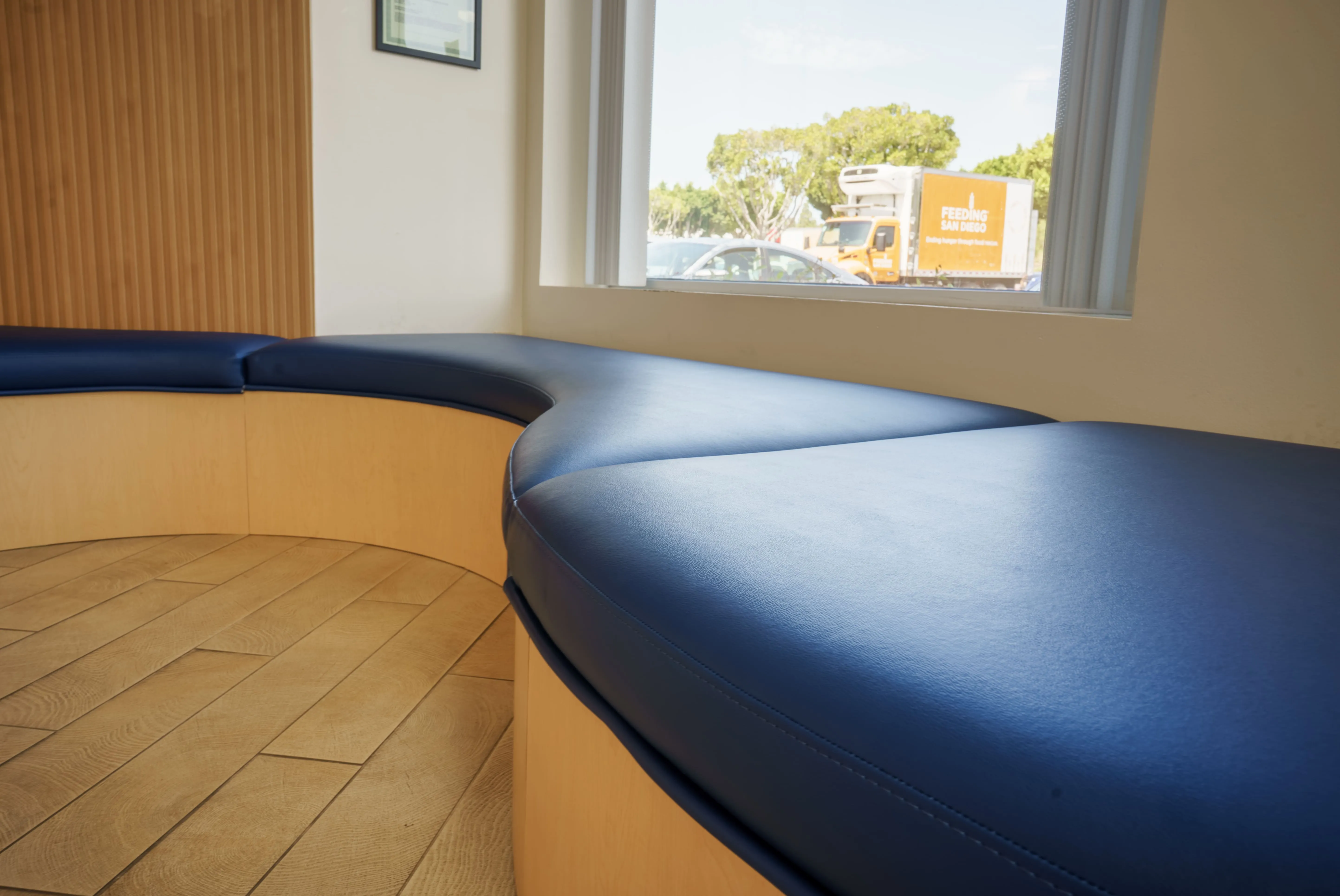 Curved navy bench seating in Feeding San Diego's lobby, with a branded Feeding San Diego delivery truck visible through the window outside