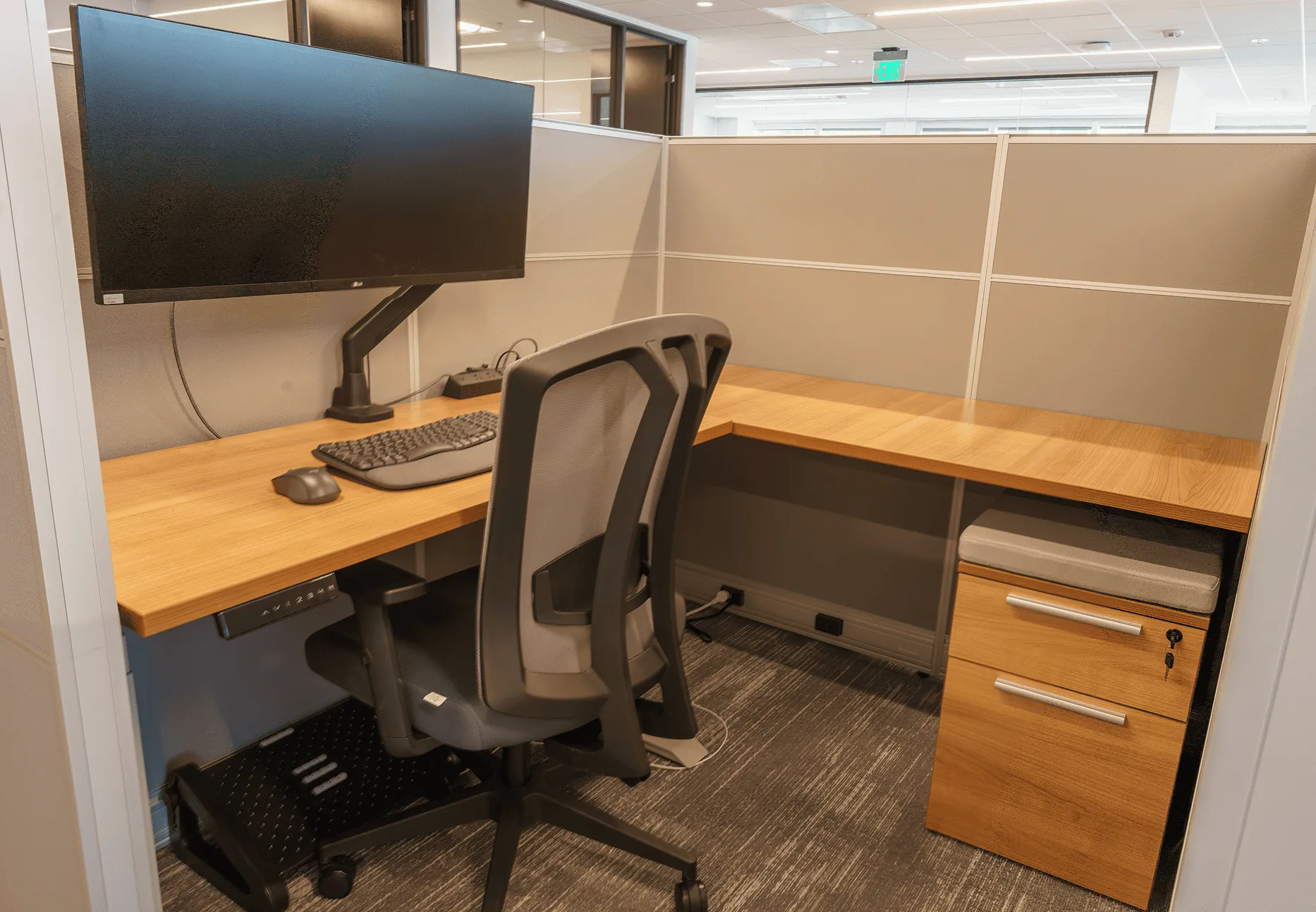 Private L-shaped office cubicle at PeopleConnect with an ultrawide monitor, ergonomic task chair, and locking file pedestal
