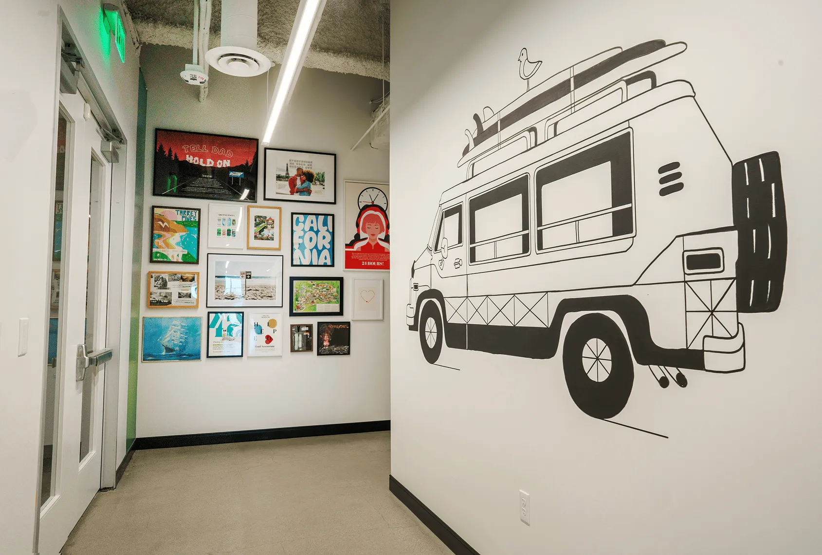 Hallway inside PeopleConnect's office with a gallery wall of framed local art next to a hand-drawn camper van and surfboard mural
