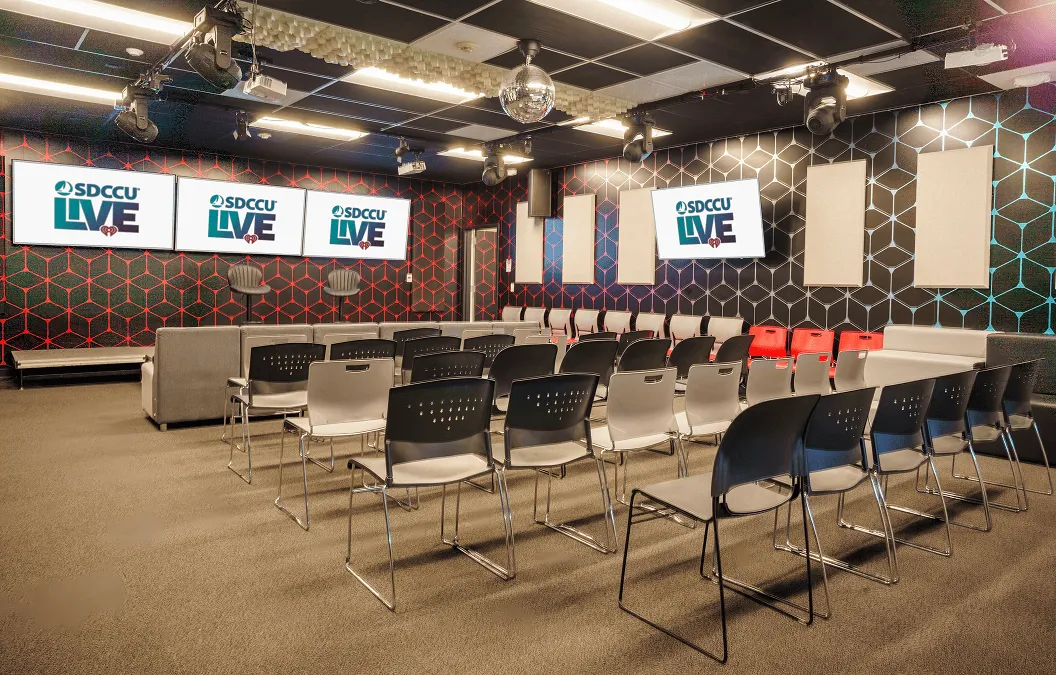 "iHeartMedia's live broadcast event space in San Diego with a disco ball, geometric accent walls, and screens displaying ""SDCCU Live"""
