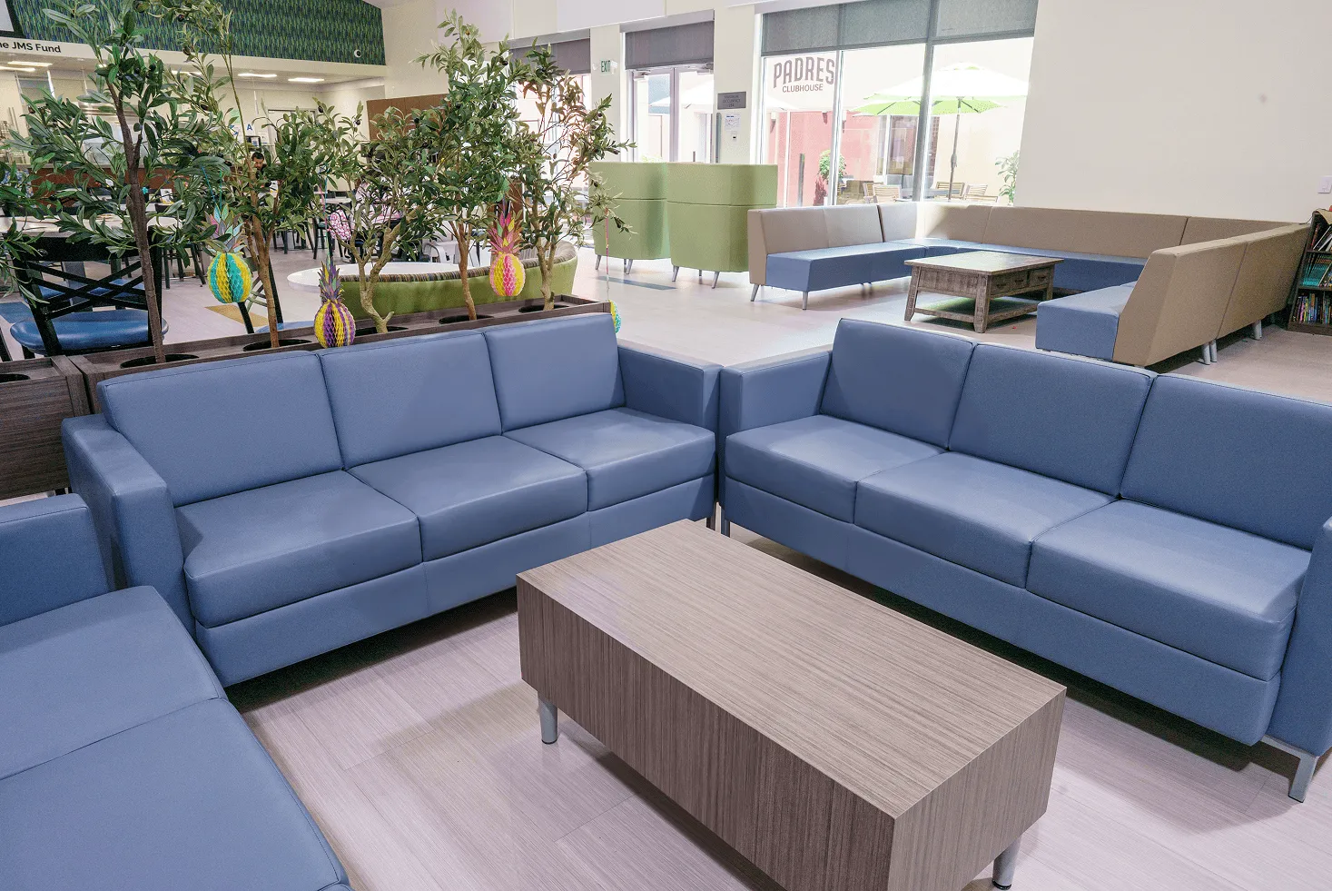 "Blue sofa seating in an indoor lounge at the Ronald McDonald House Charities San Diego campus, with the outdoor ""Padres Clubhouse"" patio visible through the window"