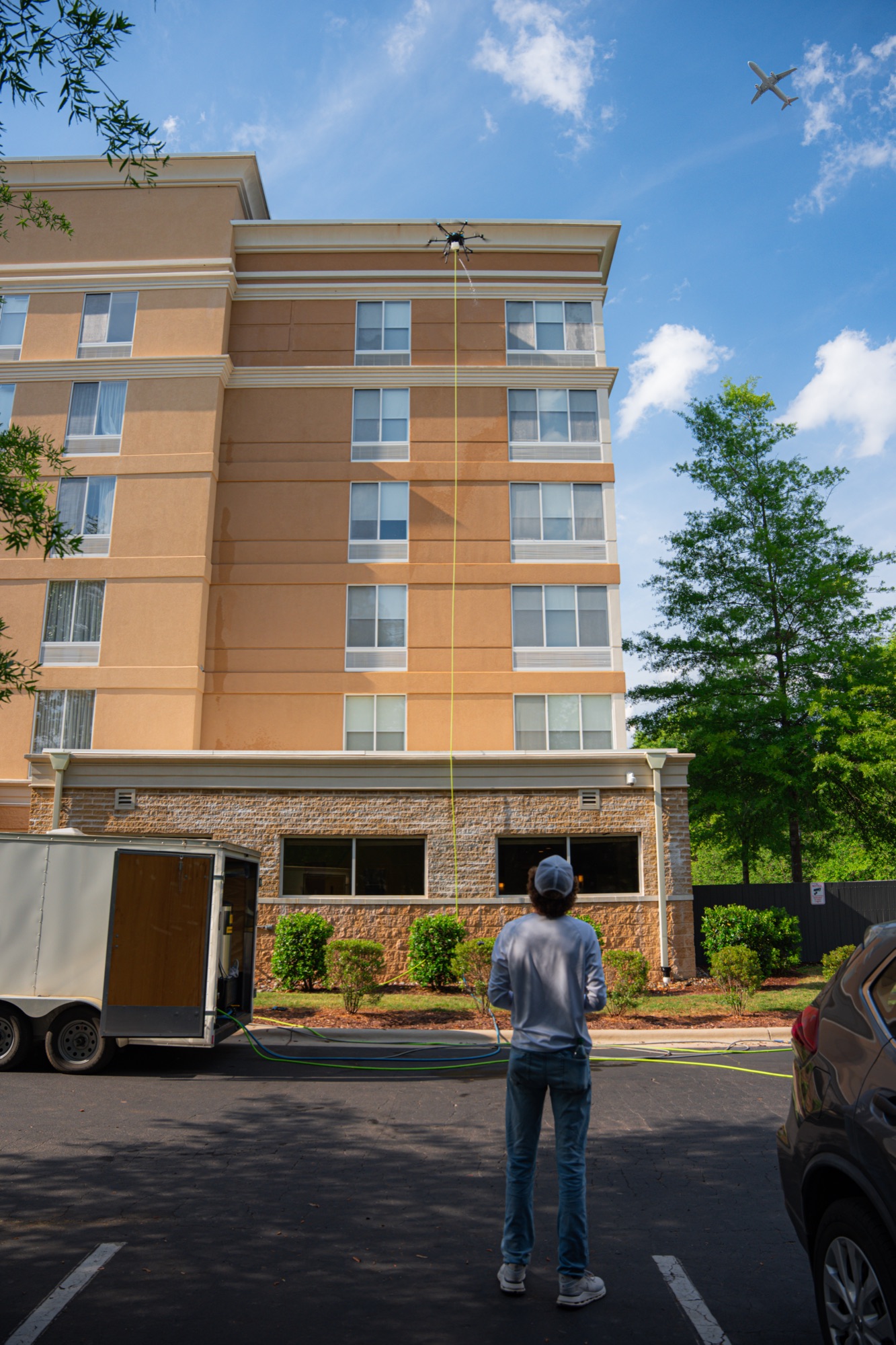 Top Flight operator standing on the ground controlling a cleaning drone that reaches the top of a multi-story hotel