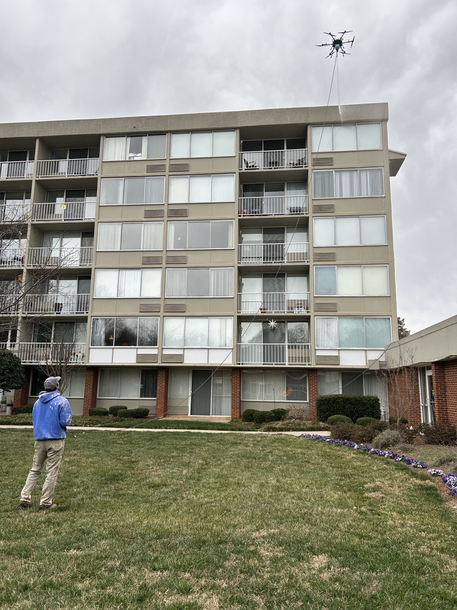 Operator on the ground controlling a cleaning drone at a multi-story multifamily building