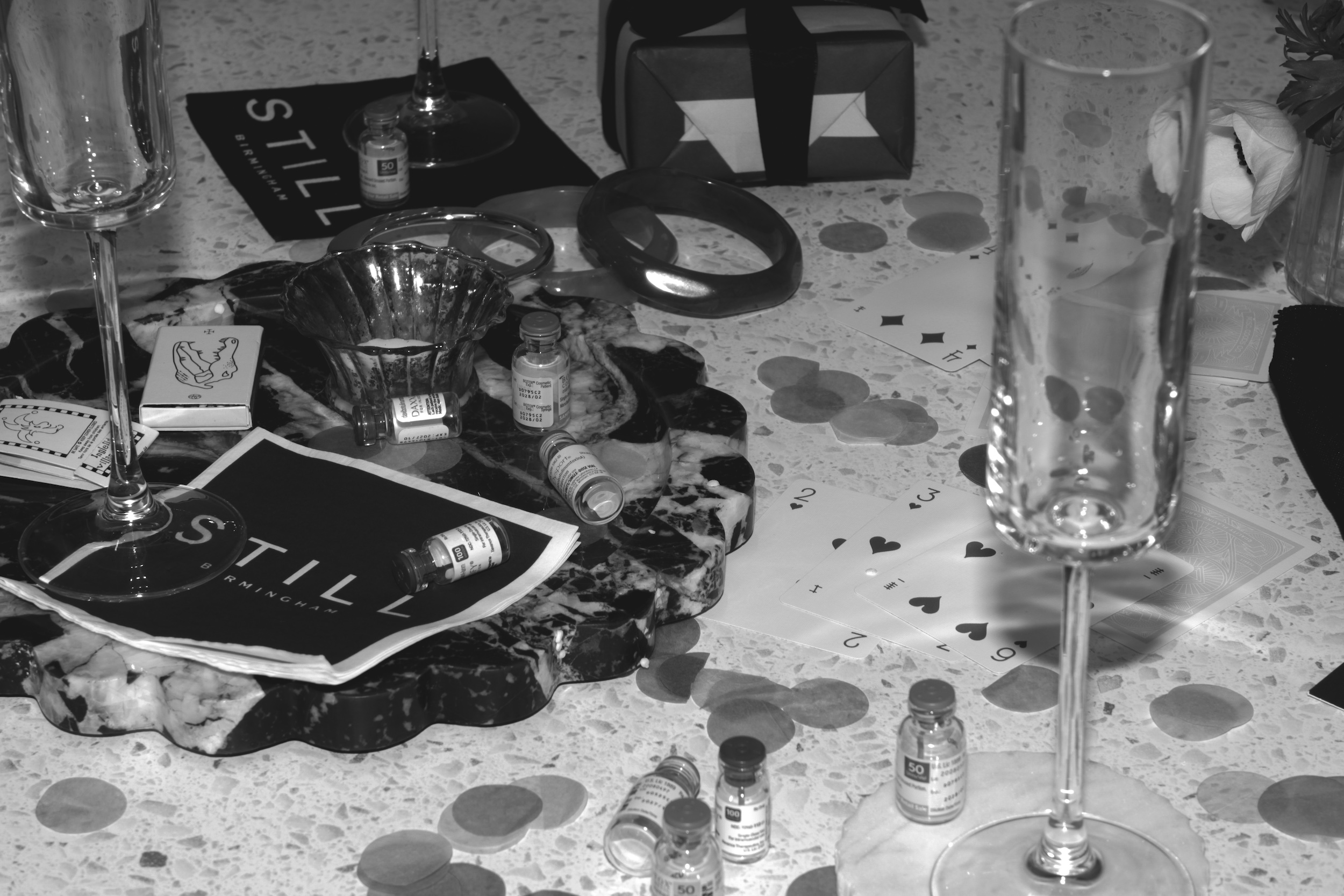 Neurotoxin vials, glassware, playing cards and confetti arranged on a marble table at a STILL Studios after-hours event