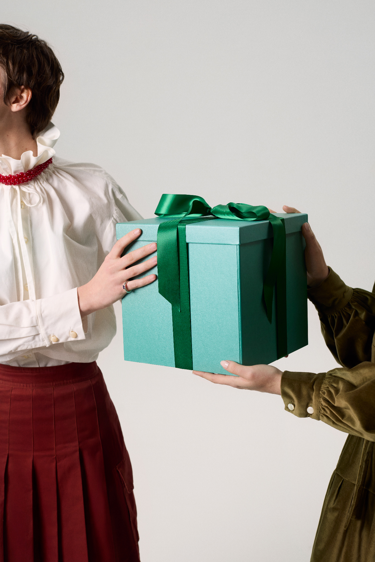 Two people exchanging a teal gift box tied with a green ribbon