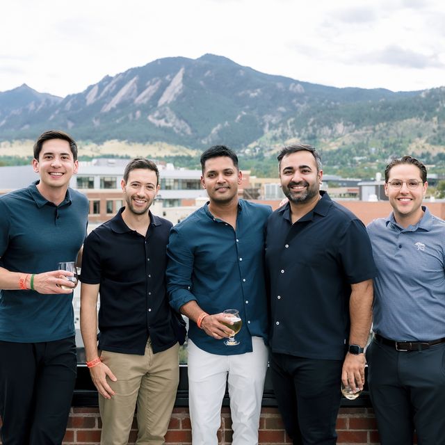 Five teammates on a Boulder rooftop with the Flatirons behind them
