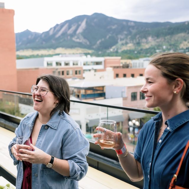 Two teammates laughing on the balcony with the Flatirons behind them