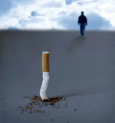 Mégot de cigarette planté dans le sable, une personne s'éloigne à l'horizon