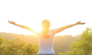 Femme les bras ouverts face au soleil dans un champ