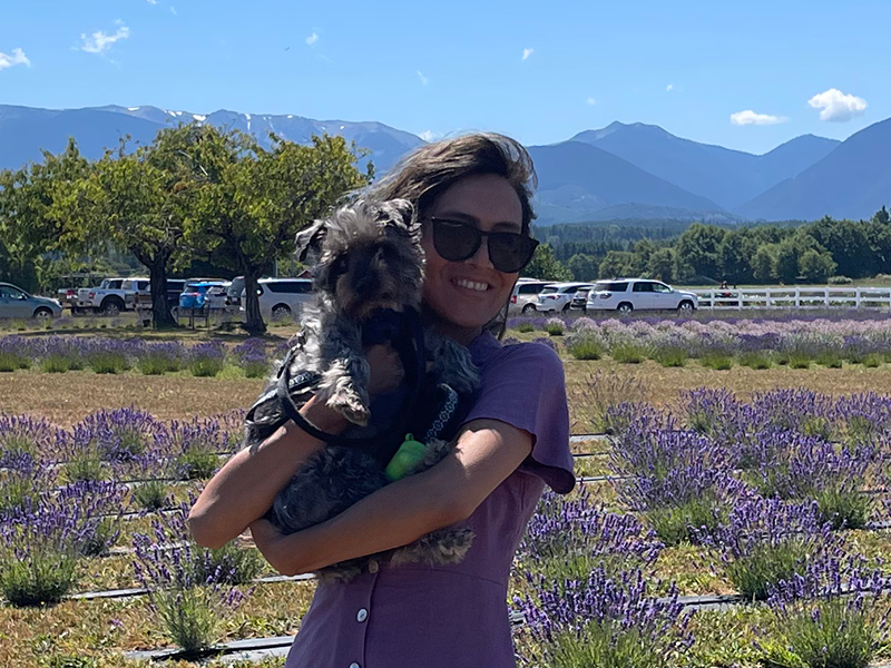 Photo of Lili and her dog in a field of lavender plants, with mountains and blue sky in the background.