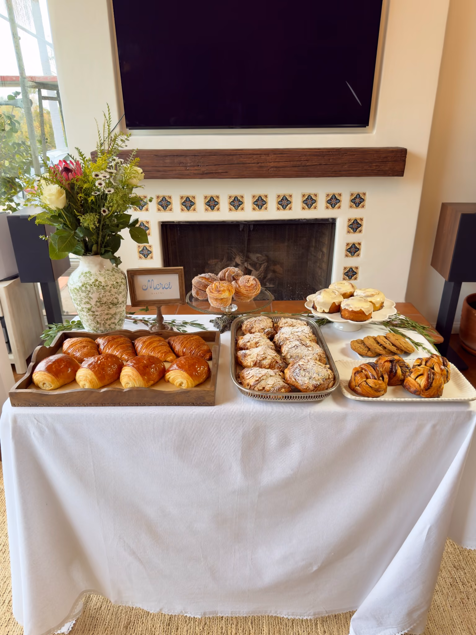 A Merci Bakery event table dressed in white linen with trays of croissants, cinnamon rolls and cruffins