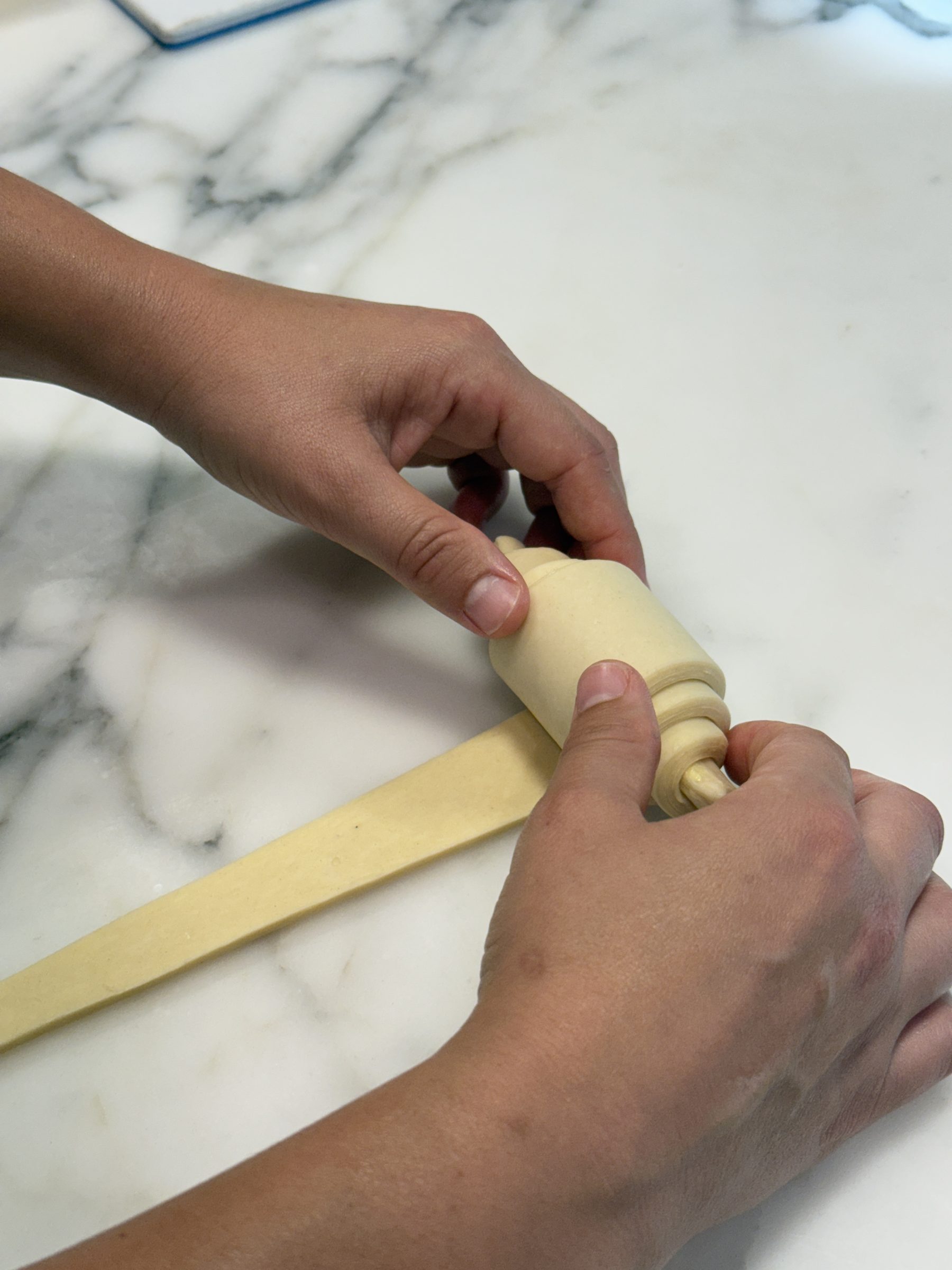 Hands rolling a strip of laminated dough into a croissant on a marble counter